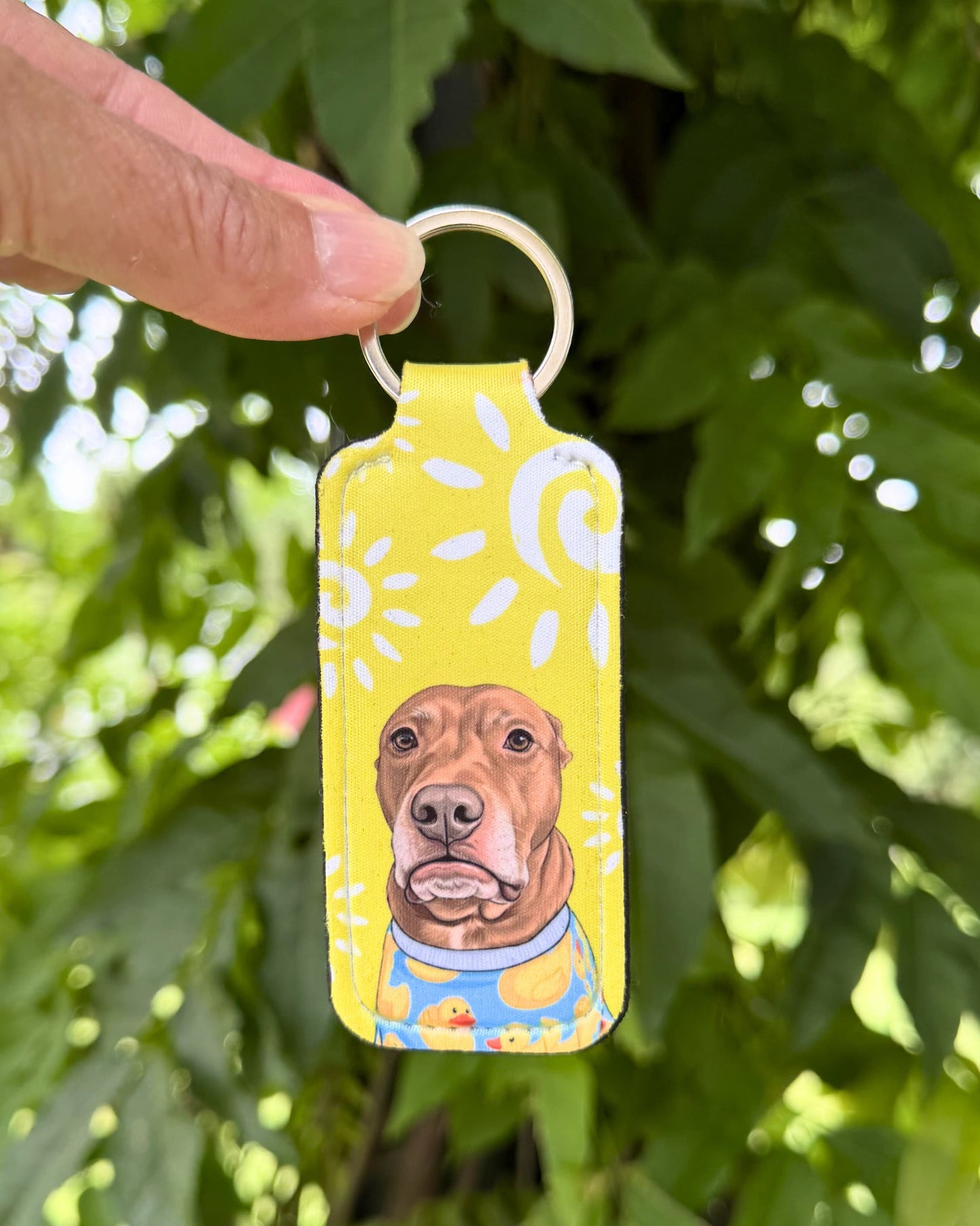 Opie lip balm holder keychain in yellow polka dot design held up outdoors, neoprene lip balm keychain with pit bull portrait, official @justopiethings merch by Sly Dawg Studio