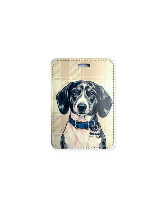 Black and silver dapple dachshund luggage tag with an original design of a doxie wearing a blue collar and a bone-shaped charm that reads "Hooligan", on a tan plaid background. Faux leather luggage tag with stitched edges and a slot at the top.