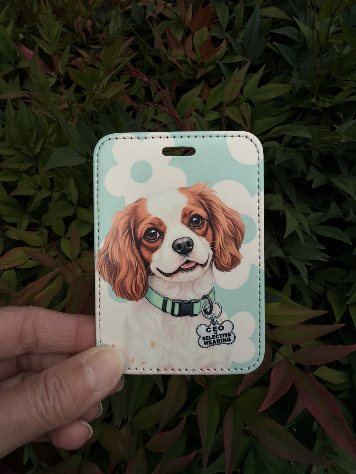 Blenheim Cavalier Luggage Tag held outdoors in front of green leaves. A Blenheim Cavalier King Charles Spaniel wears a mint collar and a charm that reads "CEO of Selective Hearing" on mint and cream flowers.