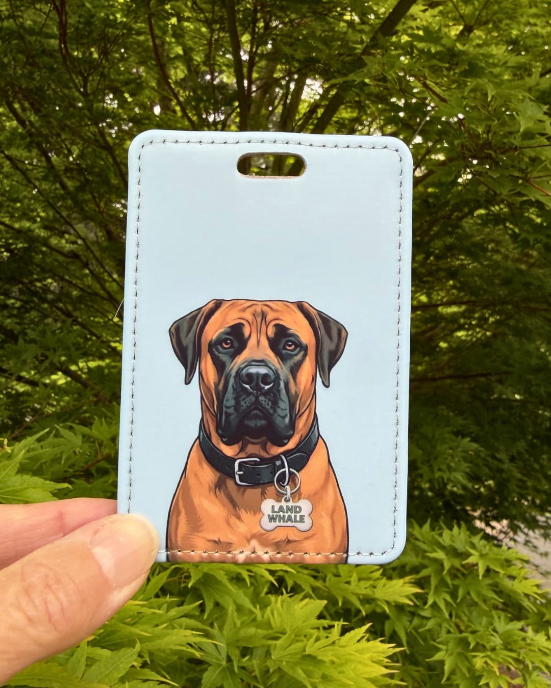 Boerboel luggage tag lifestyle; hand holding the faux leather Boerboel Land Whale luggage tag outdoors with green Japanese Maple leaves in the background.