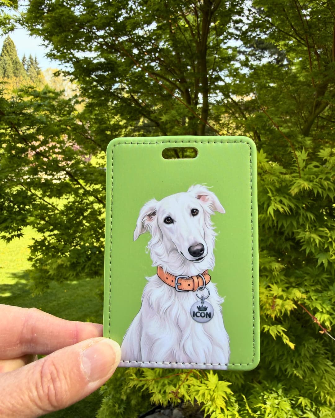 borzoi sighthound luggage tag held outdoors showing detailed white Borzoi illustration with ICON collar tag against backdrop of green maple leaves