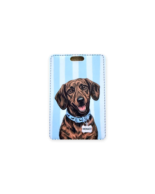 Brindle dachshund luggage tag with an original design of a doxie wearing a light blue dachshund-print collar and a bone-shaped charm that reads "Menace", on light blue stripes. Faux leather luggage tag with stitched edges and a slot at the top.