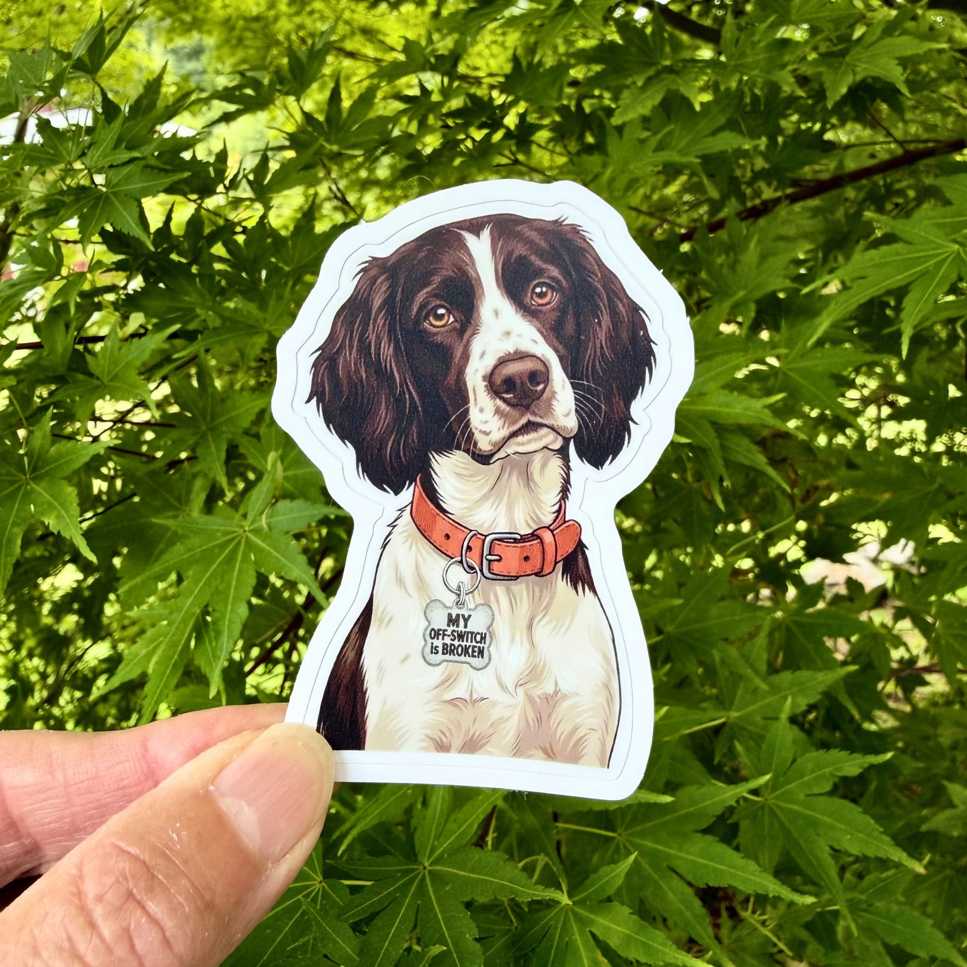 Hand holding Brittany Spaniel waterproof vinyl sticker outdoors against green foliage.