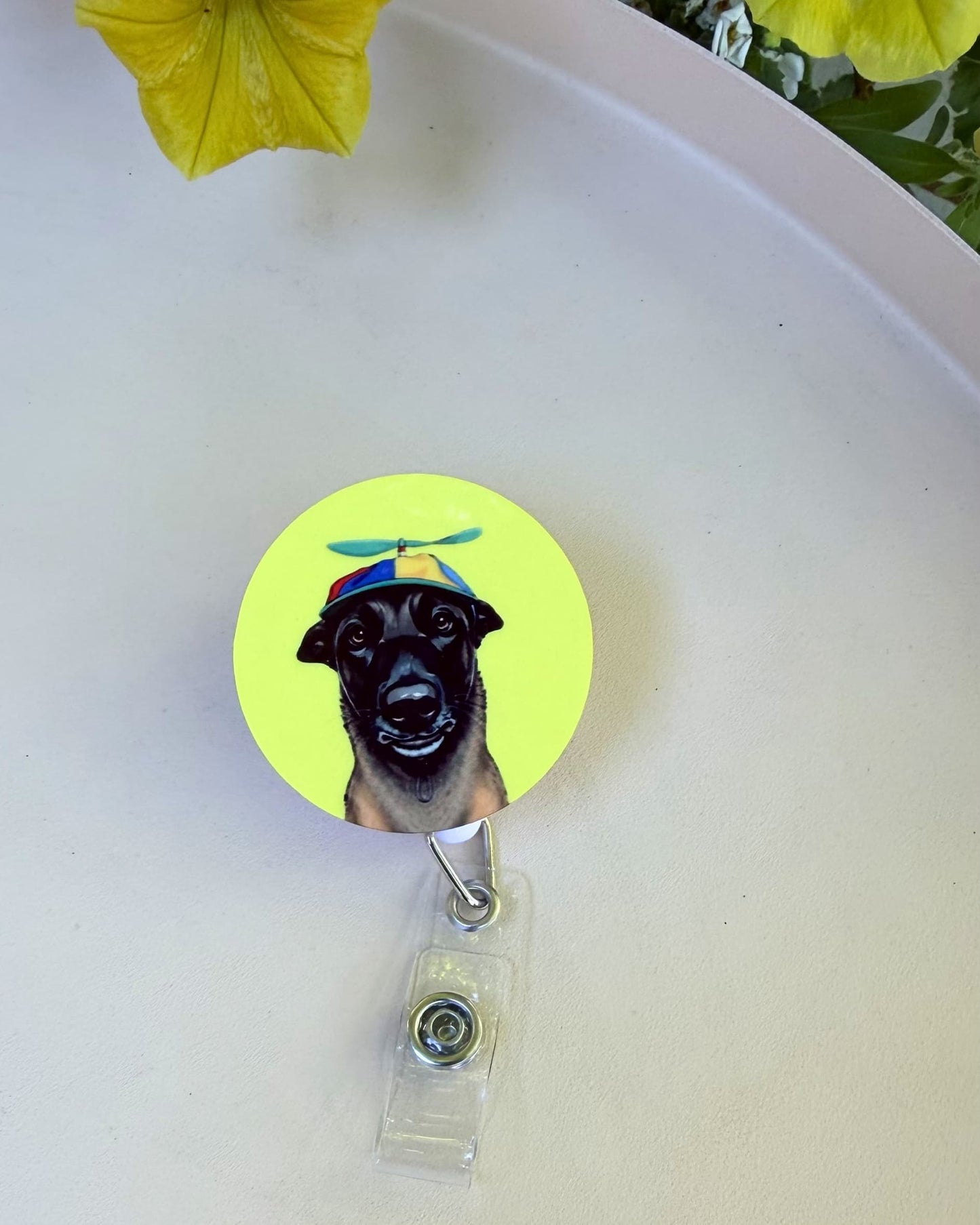 Custom dog badge reel lifestyle, retractable badge reel with illustrated black dog wearing colorful propeller hat on yellow-green background, tabletop setting