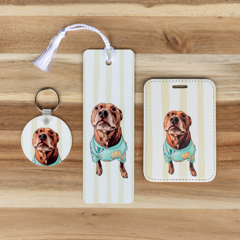 Custom pet essentials set: photo keychain, bookmark, and luggage tag featuring a stylized illustrated chocolate lab in a teal shirt, displayed on a wood background 