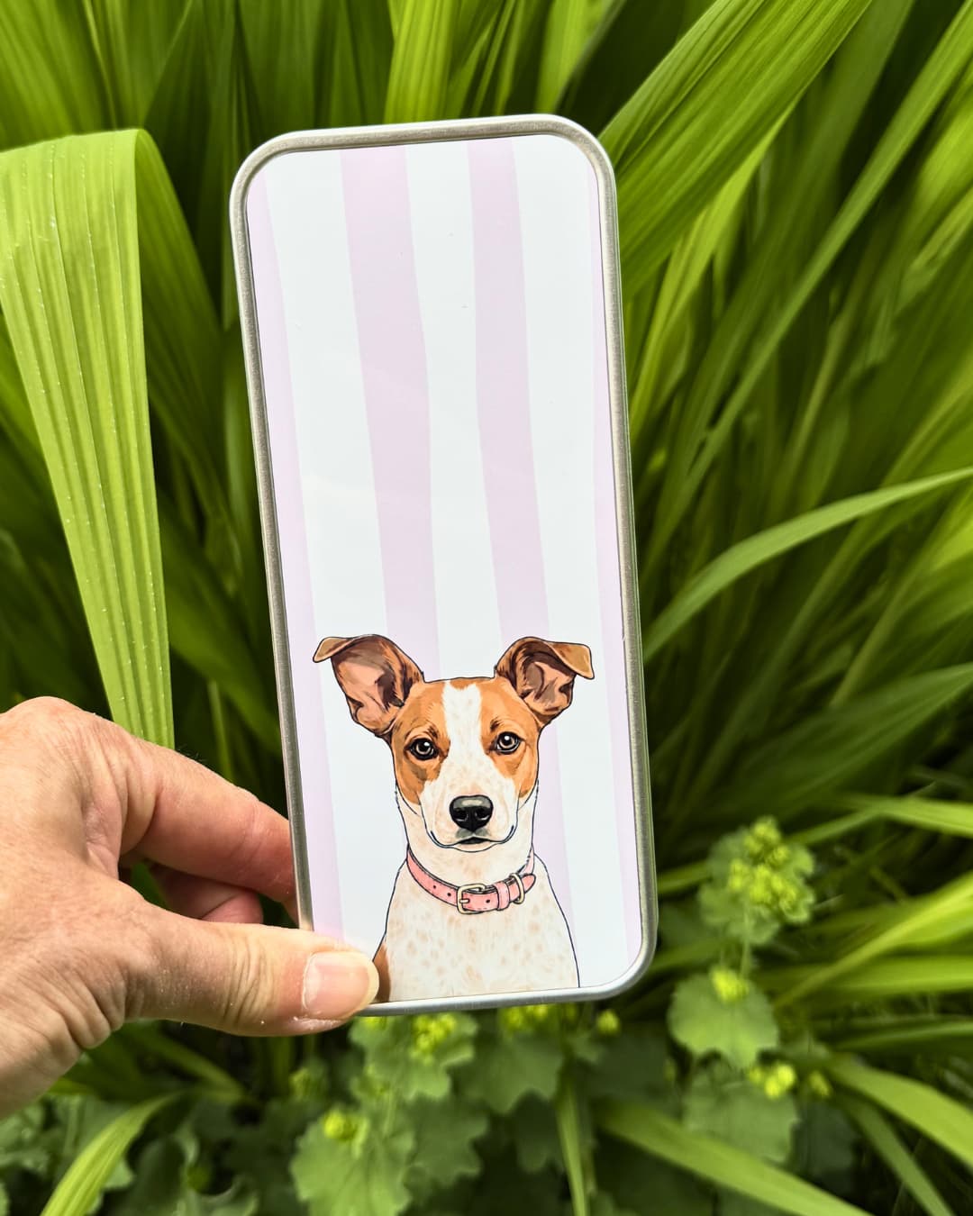 Custom pet photo storage tin held outdoors against tropical green leaves, featuring Jack Russell Terrier illustration, personalized metal organizer by Sly Dawg Studio