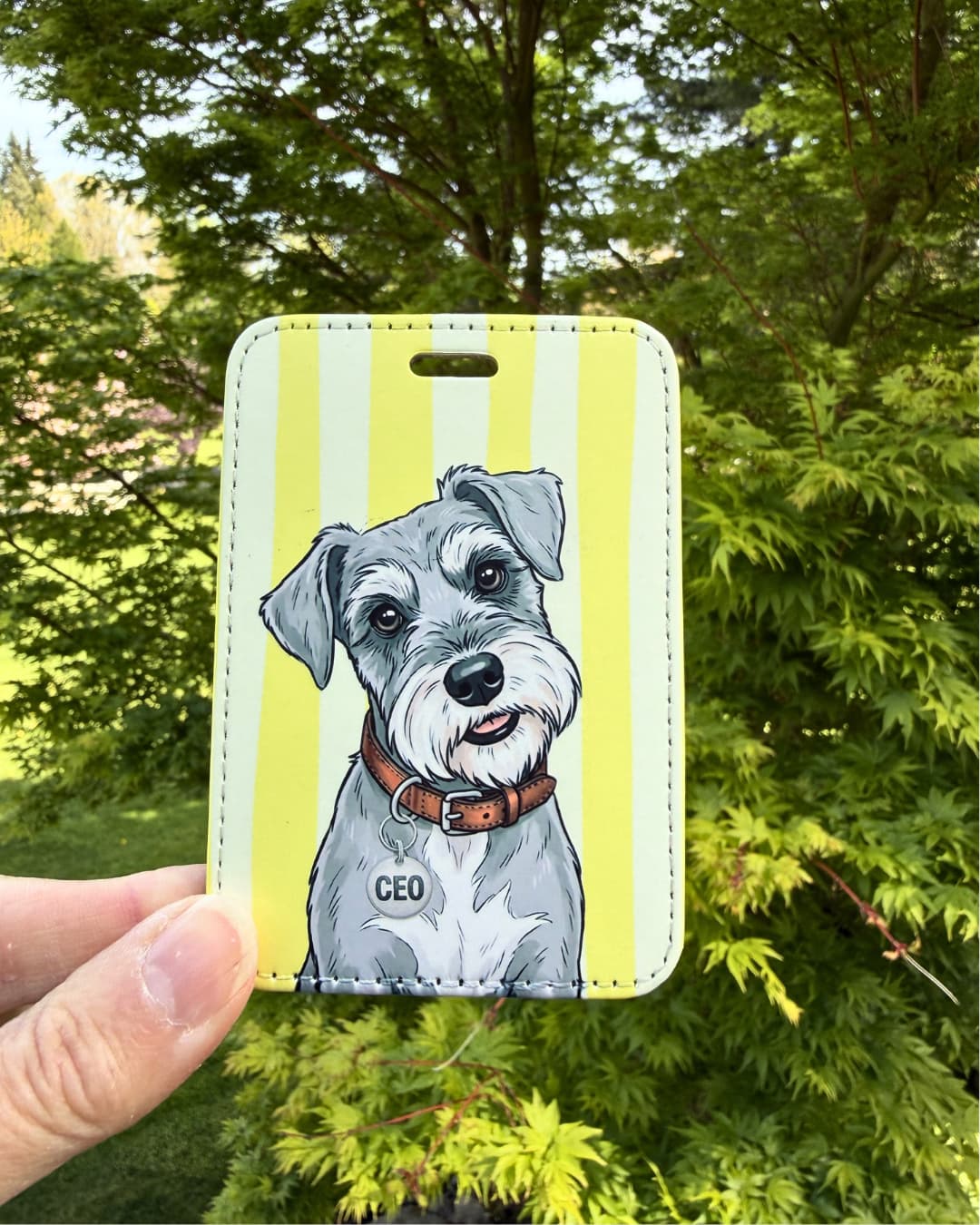 cute schnauzer luggage tag handheld lifestyle shot showing gray miniature schnauzer with CEO collar tag on yellow and white striped faux leather tag