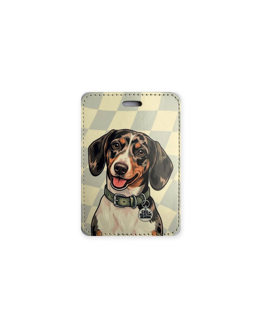 Dapple dachshund luggage tag with an original design of a smiling doxie with black, gray and tan dappled coat and white chest, wearing a sage green collar and a round charm that reads "CEO of Selective Hearing", on a cream and pale gray checkered background. Faux leather luggage tag with stitched edges and a slot at the top.