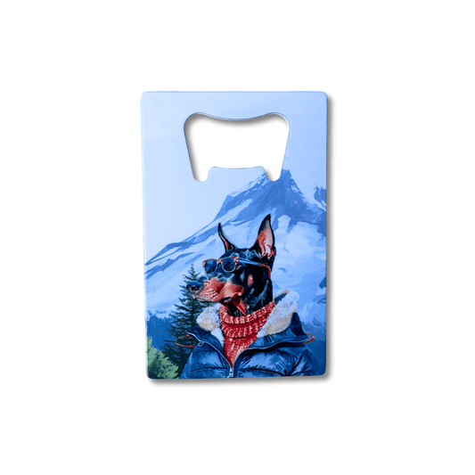 Flat stainless steel doberman bottle opener featuring an illustrated dogin outdoor gear with mountains in the background.