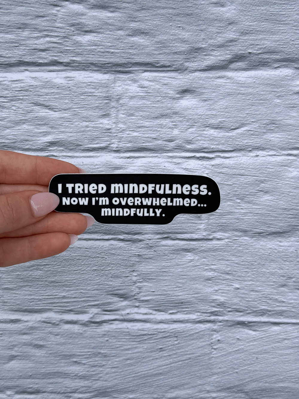 Hand holding a black and white funny mindfulness sticker with text on a gray textured background