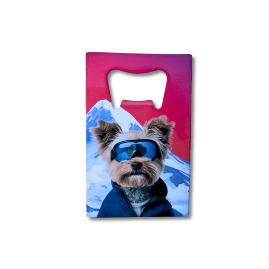 Stainless steel wallet-size Yorkie bottle opener featuring a dog wearing ski goggles in a snowy mountain scene and red sunset background. 