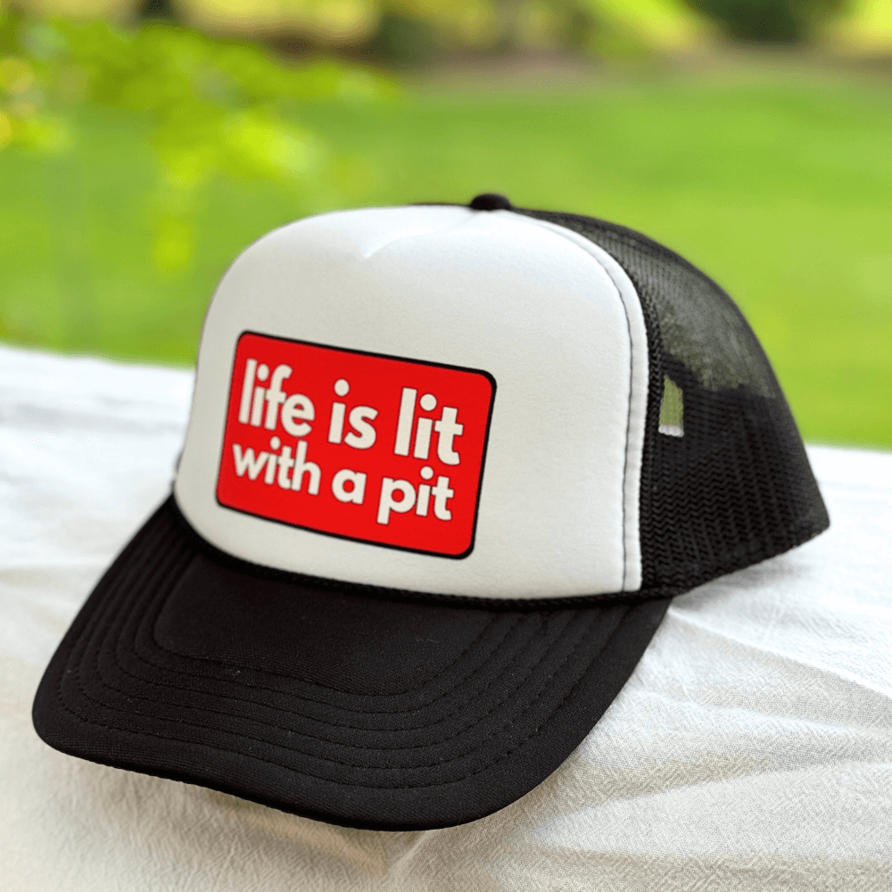 Black and white pitbull hat for humans with a red label reading 'life is lit with a pit' on a blurred green background