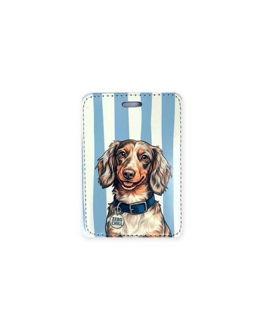 Long haired chocolate dapple dachshund luggage tag with an original design of a doxie wearing a navy collar and a round charm that reads "Zero Chill", on blue and cream stripes. Faux leather luggage tag with stitched edges and a slot at the top.