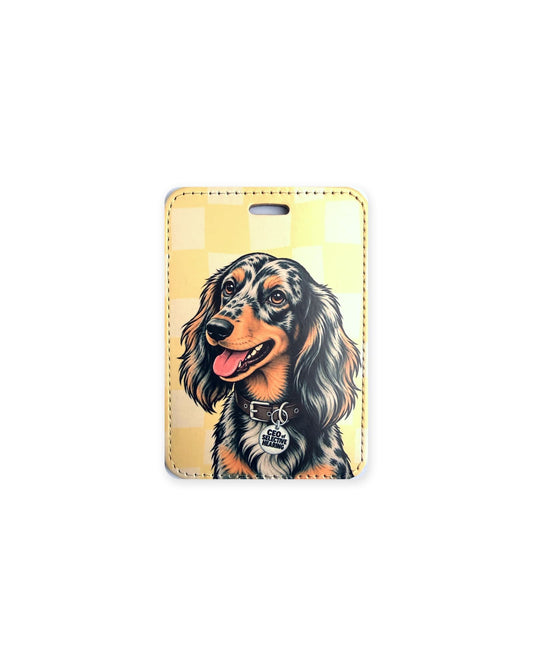 Long haired silver dapple dachshund luggage tag with an original design of a doxie wearing a brown leather collar and a round charm that reads "CEO of Selective Hearing", on a yellow checkered background. Faux leather luggage tag with stitched edges and a slot at the top.