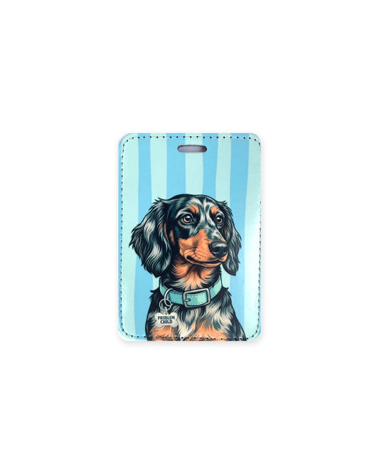 Long haired silver dapple dachshund luggage tag with an original design of a doxie wearing a light blue collar and a bone-shaped charm that reads "Problem Child", on blue stripes. Faux leather luggage tag with stitched edges and a slot at the top.