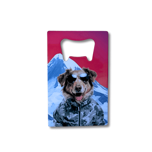 Dog Bottle Opener for Outdoor Adventures featuring mixed breed dog wearing grey camo jacket. Mountain behind dog. Red sunset sky. White background.