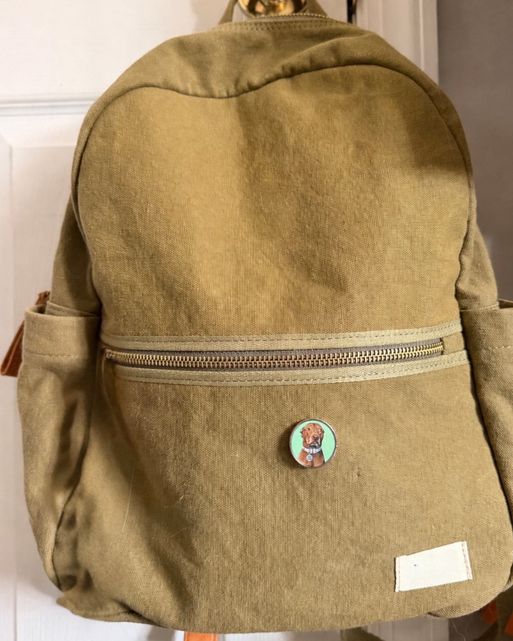 Official Opie pin clipped to olive canvas backpack, pit bull portrait pin by Sly Dawg Studio