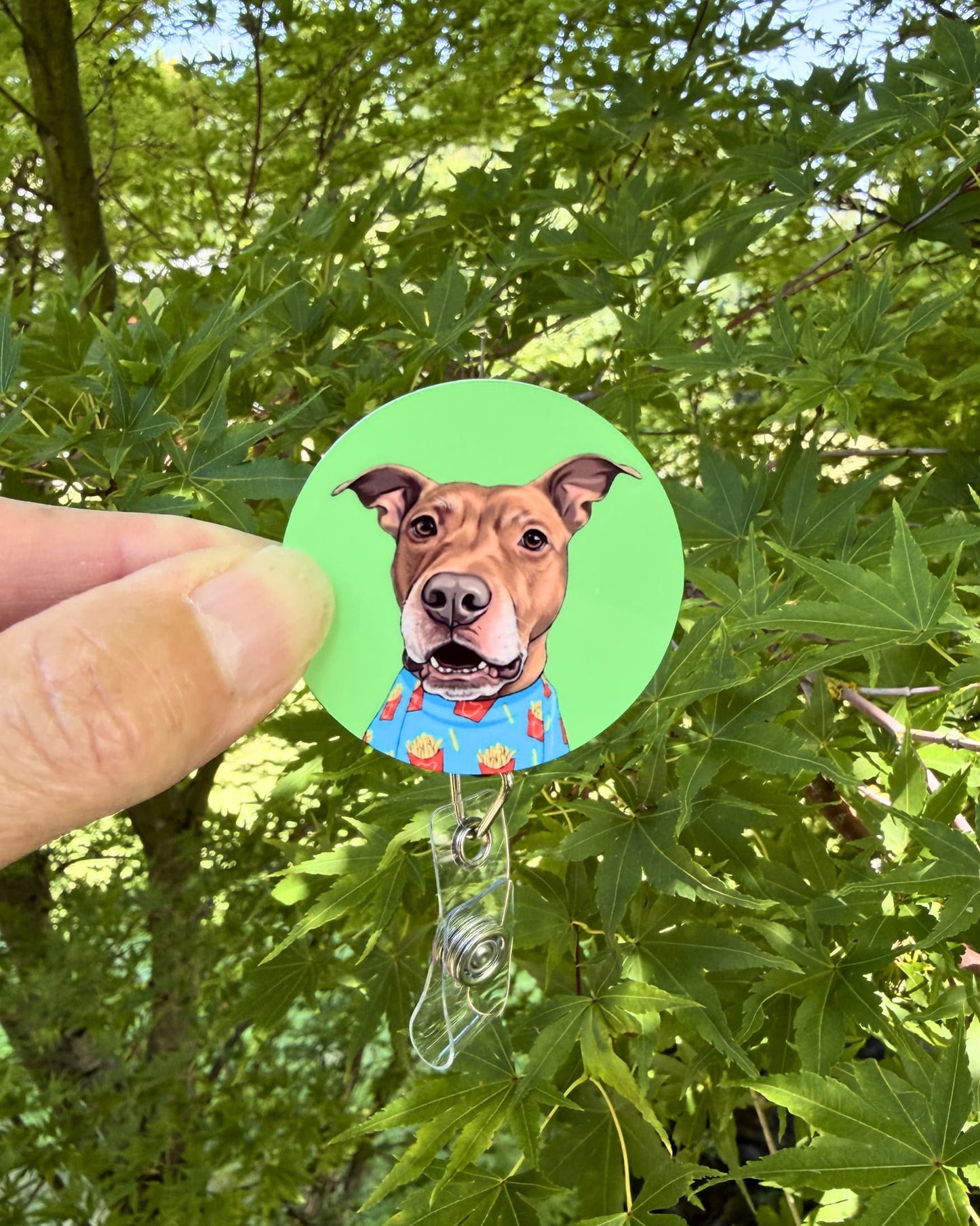Opie badge reel held outdoors, pit bull in french fry shirt on green background, retractable badge reel by Sly Dawg Studio