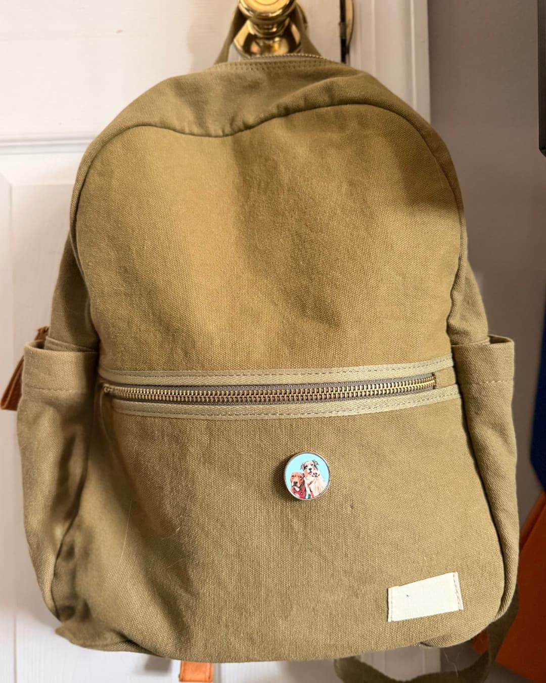 Personalized pet photo metal pin attached to khaki/olive backpack, lifestyle photo showing wearable size