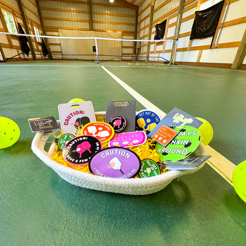 The ultimate Pickleball Lover Gift Basket: Pickleball enamel pin, hilarious Pickelball keychain, Humorous Pickleball Patch, Pickleball backpack charm or dog tag, funny pickleball stickers.