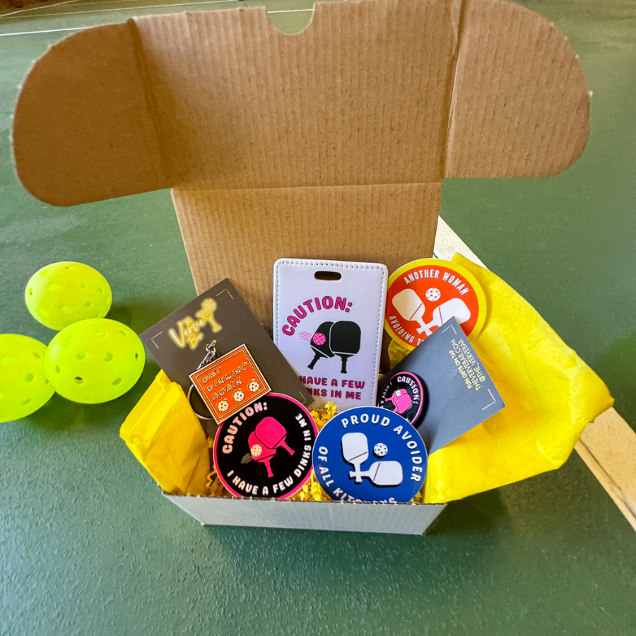 Pickleball gift box with stickers, enamel pin, keycahin and luggage tag in a shipping box with yellow tissue.