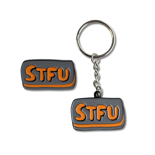 A 1.57-inch grey and orange rectangular enamel pin and matching keychain that say STFU in bold bubbly letters, representing a rude keychain and pin bundle for sarcastic gift giving.