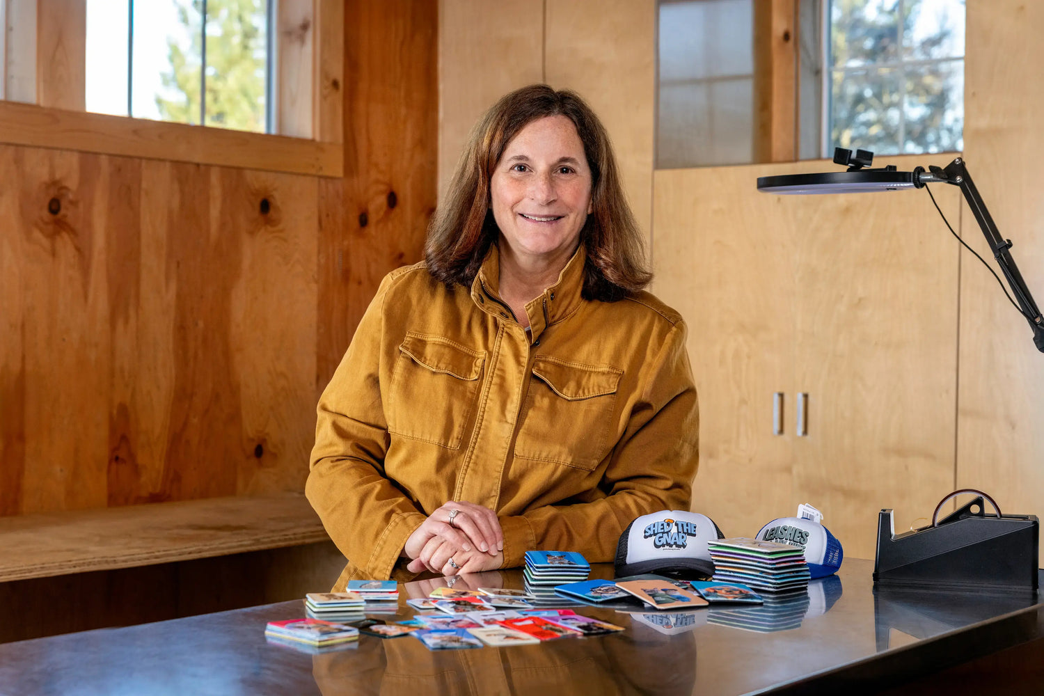 Owner of Sly Dawg Studio in her Oregon barn workshop, surrounded by custom dog stickers, personalized pet trucker hats, and magnets.